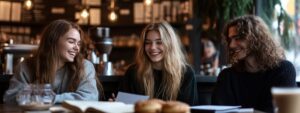 Three students laughing together over notes in a cafe.