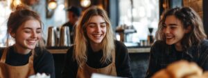 Three smiling young women in café uniforms sharing a light moment