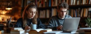 Two college students concentrating on books and laptops in a dimly lit library.