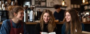Three students laughing together while reviewing notes in a coffee shop.