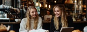 Two college students laughing while reviewing Abstract Algebra notes in a café.